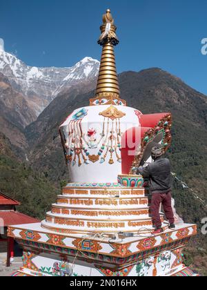 Chhomrong, Népal. Homme finissant les derniers détails de la nouvelle stupa de village. Annapurna Sud en arrière-plan. Banque D'Images