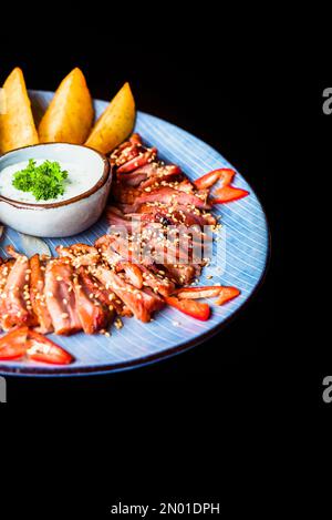 Filet d'oie frit à l'ail servi avec des quartiers de pommes de terre et du kim chi sur fond noir vue du dessus Banque D'Images