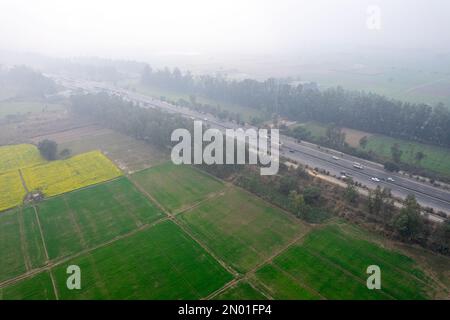 un drone aérien a tiré dessus des feuilles de moutarde jaune et vert vers une grande autoroute occupée perdue dans le brouillard près du rajassan punjab Banque D'Images