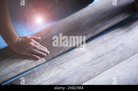 Installation de plancher laminé, détails sur les mains d'homme tenant des carreaux de bois, sur la couche de base en mousse blanche, petite pile avec plus de tuiles arrière-plan Banque D'Images