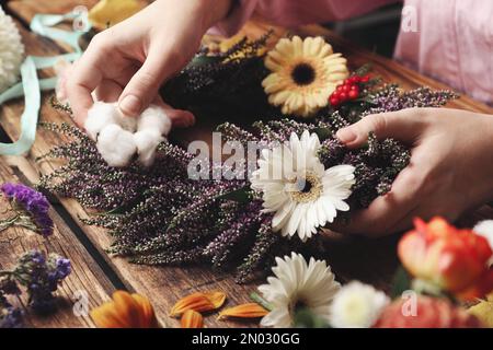 Fleuriste faisant belle couronne automnale avec des fleurs chinées à table en bois, gros plan Banque D'Images