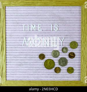 Expression - le temps, c'est de l'argent - écrit à partir de lettres blanches sur le tableau de lettres. Les pièces de monnaie de différents pays sont disposées à proximité. Fond rose. Vue de dessus. Banque D'Images