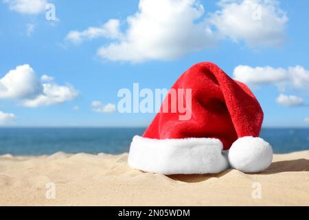 Chapeau de Santa sur la plage de sable, espace pour le texte. Vacances de Noël Banque D'Images