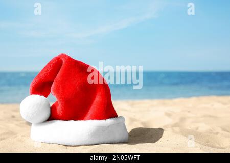 Chapeau de Santa sur la plage de sable, espace pour le texte. Vacances de Noël Banque D'Images