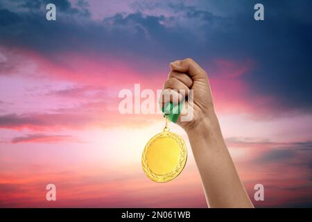 Gagnant levant la main avec la médaille d'or jusqu'au ciel du coucher du soleil, gros plan Banque D'Images