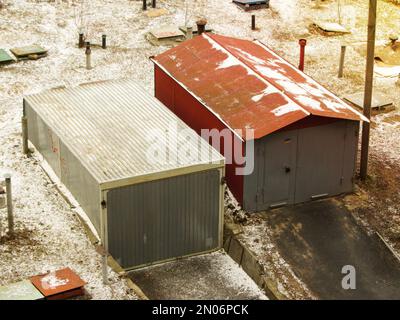 Deux vieux garages de voitures en métal comme vu d'en haut en hiver. Un vieux garage en métal rouge gris sur un mur de clôture dans une rue rurale. Ancienne porte métallique Banque D'Images