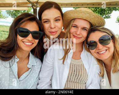 Photo en plein air de quatre jeunes femmes qui s'amusent dans une rue de la ville et prennent un selfie. Les amies multiraciales aiment passer une journée en ville. Banque D'Images