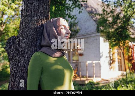 Jeune fille musulmane embrassant un arbre. Gros plan d'une jeune femme dans un hijab et de vêtements décontractés dans le parc. Protéger l'environnement et les soins Banque D'Images