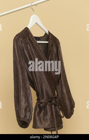Vêtements pour femmes. Porte-vêtements avec élégant et élégant chemisier en soie marron sur cintre. Article de mode intemporel de bonne qualité. Banque D'Images