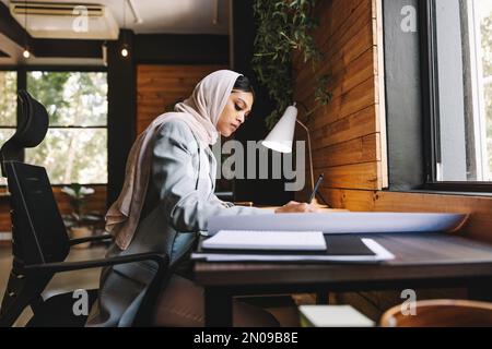 Un designer musulman fait de nouveaux dessins architecturaux dans un bureau moderne. Jeune femme d'affaires créative qui planifie un projet novateur. Femme architecte nous Banque D'Images