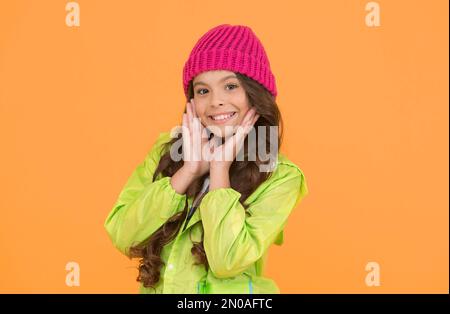 Choisissez entre le plus mignon et le plus tendance. Enfant fille vêtements bonnet tricoté. Accessoire chapeau d'hiver. Fille cheveux longs fond jaune. Concept de saison froide. Hiver Banque D'Images