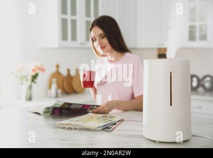 Humidificateur d'air moderne et femme floue buvant du café dans la cuisine Banque D'Images