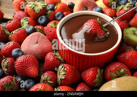 Fourchette à fondue avec fraise dans un bol de chocolat fondu entouré d'autres fruits sur la table Banque D'Images