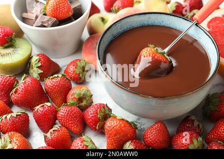 Fourchette à fondue avec fraise dans un bol de chocolat fondu entouré d'autres fruits sur la table Banque D'Images