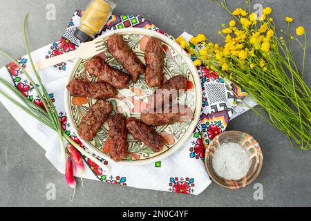 rouleaux de viande traditionnels, appelés “mititei” sur une assiette en céramique, avec un bouquet de fleurs de coupe de beurre Banque D'Images