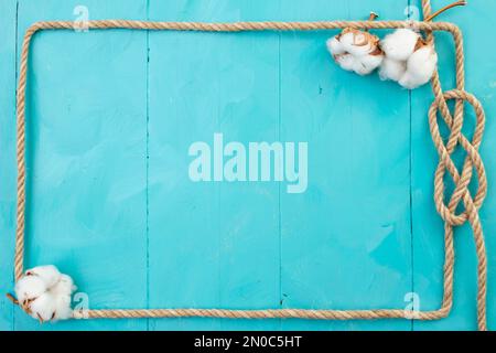 Cadre rectangulaire en corde de jute, avec noeud et fleurs de coton, sur des planches peintes en bleu, toile de fond bleu marine Banque D'Images