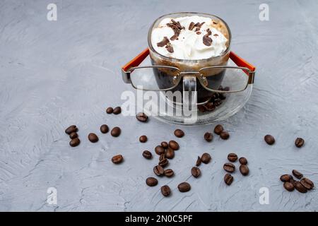 Tasse de café en verre avec crème fouettée et grains de café. Café, et lecture de lunettes sur texture gris de ciment. Banque D'Images