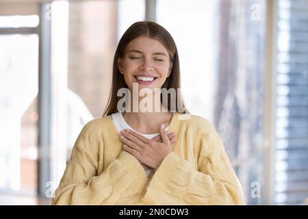 Bonne jolie jeune femme appliquant les mains à la poitrine avec gratitude Banque D'Images