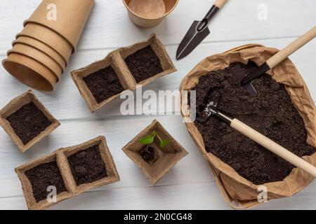 Outil de jardin dans un sac en papier avec de la terre. Pots de tourbe et de papier avec terre. Pose à plat. Arrière-plan blanc. Banque D'Images