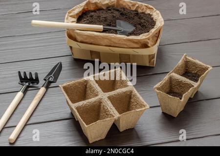 Pelle de jardin dans un sac en papier avec de la terre. Râteler, pelle et pots de tourbe. Vue de dessus. Arrière-plan en bois sombre. Banque D'Images