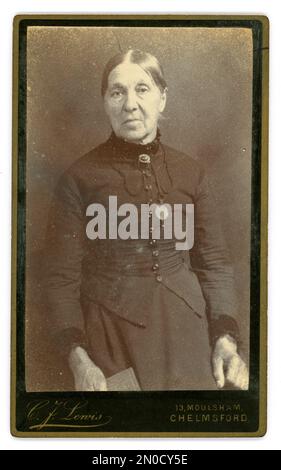 Original, clair avec beaucoup de détails du visage et des vêtements, l'ère victorienne CDV (carte de visite ou carte de visite) portrait de studio de femme plus âgée, avec une coiffure soignée de pain, qui est probablement en classe de travail avec son expression cartonnée et portant son dimanche le plus beau vêtements pour la photographie. Du studio de C F. Lewis, Moulsham, Chelmsford, Essex. ROYAUME-UNI Vers 1886 à 1890 Banque D'Images