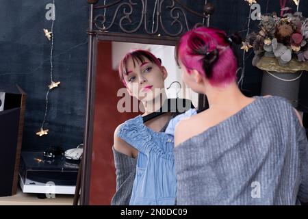 une adolescente regarde dans le miroir à l'intérieur tout en essayant une robe Banque D'Images