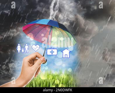 Agent d'assurance protégeant les illustrations avec parapluie arc-en-ciel de la tempête, gros plan Banque D'Images