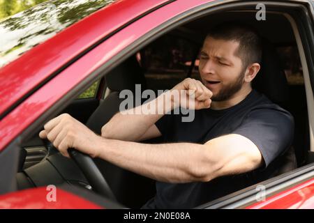 Un homme fatigué bâilling en conduisant sa voiture moderne Banque D'Images