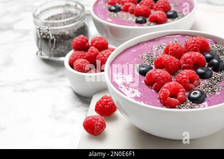 Délicieux smoothie d'acai aux framboises et aux graines de chia dans un bol sur une table en marbre blanc, en gros plan Banque D'Images