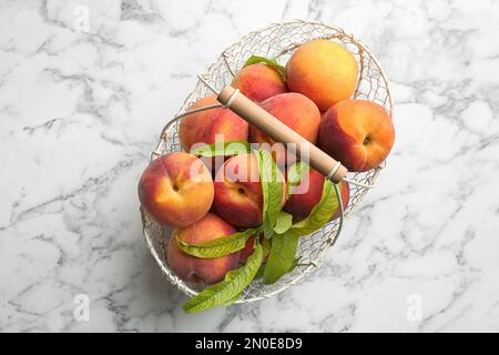 Pêches fraîches et sucrées dans un panier en métal sur une table en marbre blanc, vue du dessus Banque D'Images