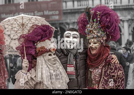 Carnaval de Venise. Un homme en masque anonyme pose avec une femme déguisée masquée avec un parasol et un homme costumé masqué avec un chapeau avec des pierres précieuses Banque D'Images
