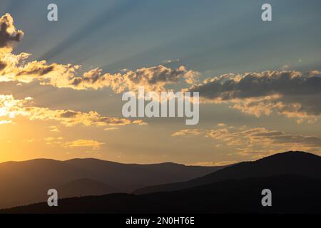 Un lever de soleil éblouissant illumine les sommets des montagnes, tandis que des rayons de soleil dorés traversent les nuages, projetant une lumière chaude. Banque D'Images