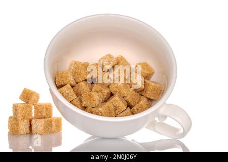 Plusieurs cubes de sucre brun dans une tasse en céramique blanche, en gros plan, isolés sur du blanc. Banque D'Images