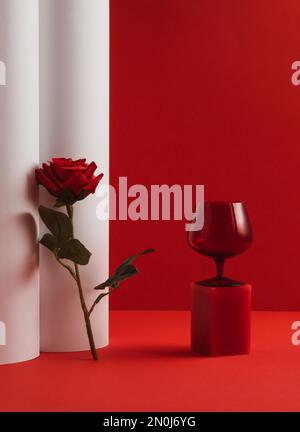 Composition créative de la Saint-Valentin avec verre rouge et fleur de rose rouge sur fond rouge et blanc. Concept de fête de printemps ou d'été de luxe minimal. Banque D'Images