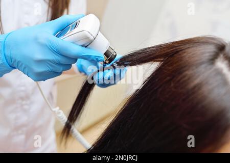 médecin cosmetologue dermatologue diagnostique l'état des cheveux du patient à l'aide d'un dispositif spécial - un trichoscope. Banque D'Images