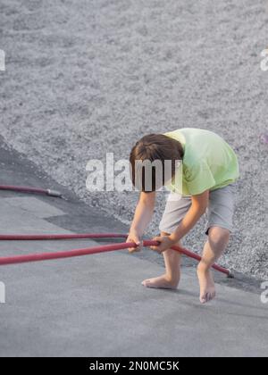 Garçon monte sur une pente de béton de sports et de terrain de jeu modernes pour enfants. Kid surmonte la peur et apprend de nouvelles choses. Activités de loisirs en plein air. Banque D'Images