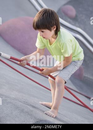 Garçon monte sur une pente de béton de sports et de terrain de jeu modernes pour enfants. Kid surmonte la peur et apprend de nouvelles choses. Activités de loisirs en plein air. Banque D'Images