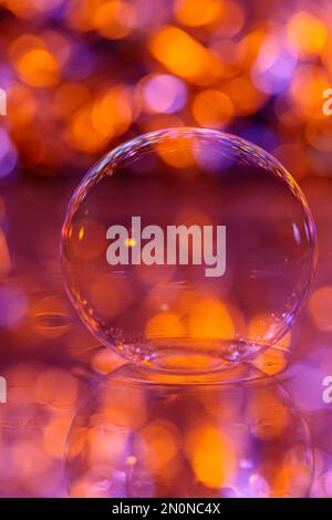 Une bulle de savon se trouve à la surface de l'eau sur fond rouge-orange Banque D'Images