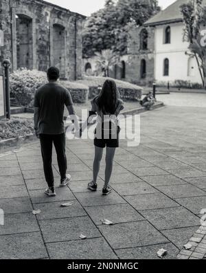 Une vue en niveaux de gris d'un beau couple marchant et tenant les mains dans le quartier historique d'Intramuros à Manille, Philippines Banque D'Images