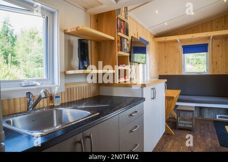 Comptoir de cuisine arborite noir avec armoires en mélamine grise et blanche, coin salon principal avec table à manger extensible en pin à l'intérieur de la mini maison. Banque D'Images