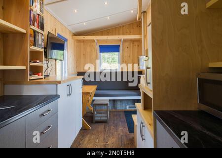 Comptoirs de cuisine arborite noir, armoires en mélamine grise et blanche et vue sur le salon principal avec table à manger extensible en pin dans mini-maison. Banque D'Images