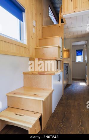 Escalier en bois de pin menant à la chambre à coucher de l'étage supérieur, coin cuisine et porte de salle de bains en arrière-plan à l'intérieur de la mini-maison mobile de 8 x 24 pieds. Banque D'Images