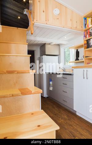 Escalier en bois de pin menant à la chambre à coucher de l'étage supérieur, coin cuisine et porte de salle de bains en arrière-plan à l'intérieur de la mini-maison mobile de 8 x 24 pieds. Banque D'Images