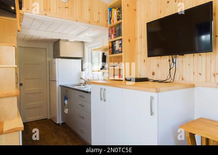 Vue partielle des escaliers en bois de pin menant à la chambre à coucher à l'étage supérieur, coin cuisine et porte de salle de bains en arrière-plan à l'intérieur de la mini-maison mobile de 8 x 24 pieds. Banque D'Images