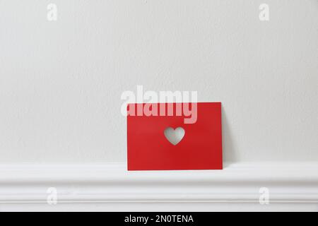 Carte de vœux rouge de Saint Valentin avec coeur découpé appuyé contre un mur blanc. Vacances du 14th février. Amour, passion concept. Fête des mères Banque D'Images