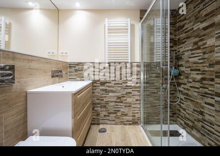 Salle de bains avec évier en porcelaine blanche au-dessus de la commode avec tiroirs en bois, miroir sans cadre sur le mur et cabine de douche vitrée Banque D'Images