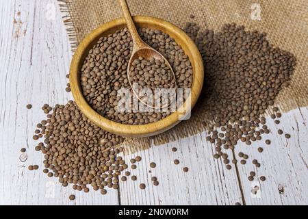 Un bol en bambou rempli de lentilles séchées sur une table blanche Banque D'Images