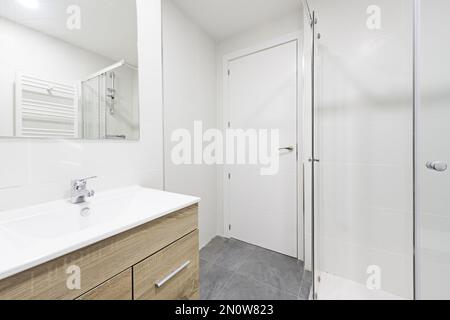salle de bains avec lavabo en bois sous un miroir mural sans cadre, douche à l'italienne avec cloisons et portes en bois blanc Banque D'Images