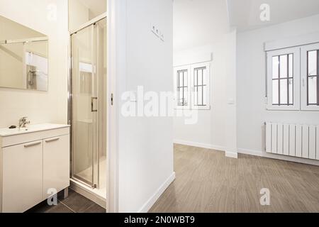 cette chambre vide comprend une paire de fenêtres en aluminium blanc avec des barres de métal et l''accès à une salle de bains dotée d''un mobilier blanc et d''une cabine de douche Banque D'Images