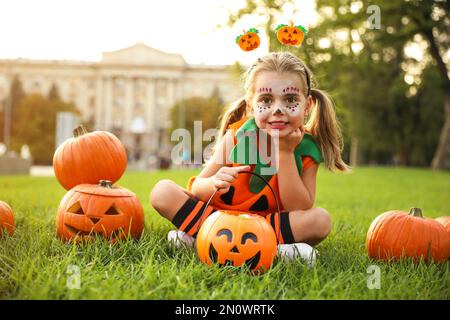 Petite fille mignonne avec un seau à bonbons de citrouille portant un costume d'Halloween dans le parc Banque D'Images